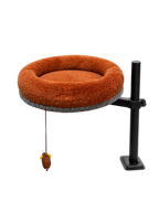Side view of the Petyze adjustable cat desk bed featuring a plush burnt-brown donut cushion with gray woven base, mounted on a black metal pole with clamp arm and desk-edge clamp, plus a small hanging mouse toy under the bed.