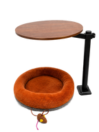 Modern cat desk bed with a plush bright-brown donut cushion mounted on a black metal stand beneath a round wooden tabletop, featuring a hanging mouse toy at the front.